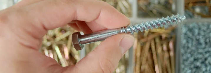 Hand hält Schraube über Schraubenbox